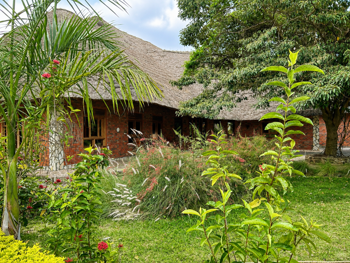 Thatched lodge buildings among palms in the gardens at Warujojo Safari Lodge, Rubirizi, Uganda