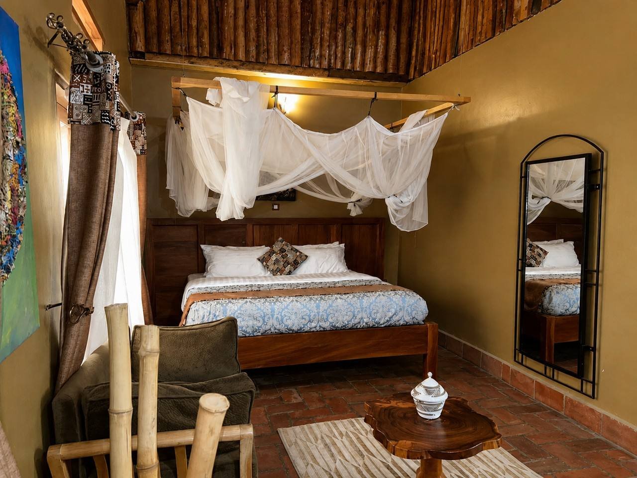 Rekemire banda at Warujojo Safari Lodge: canopied bed and open-plan lounge in ochre tones